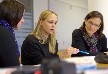 3 personer som ser på en bok som personen i midten peker på med en penn. Foto.