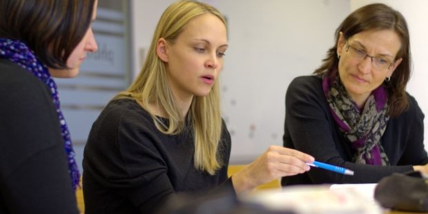 3 personer som ser på en bok som personen i midten peker på med en penn. Foto.