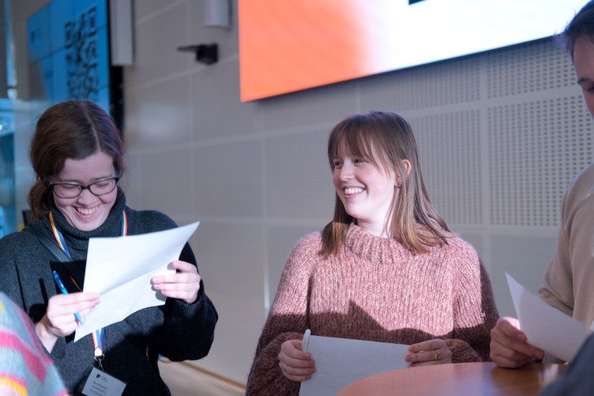 Bilde fra Pedagogstudentenes tillitsvalgtkonferanse. To kvinner står med ark og snakker i en gruppe. De smiler og ler. Foto. 