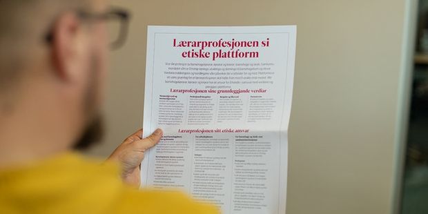 Mannsperson sitter og leser en plakat av lærerprofesjonens etiske plattform.