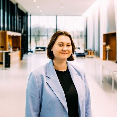 Kaspara Halkjelsvik. Kvinne, med mørkt hår til skuldrene, hun smiler mot kamera. Hun har på seg en svart t-skjorte og en lys blå blazer over. Foto: Adrian Castillo.