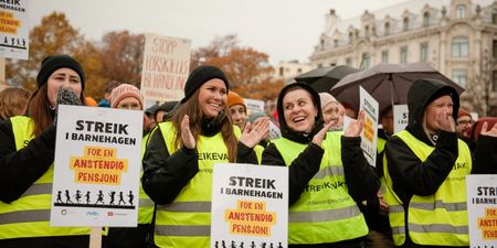 En rad med streikende barnehageansatte (kvinner) som klapper og smiler på markeringen foran Stortinget, med streikeplakater. 