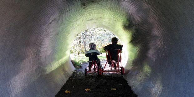 To barn som sykler gjennom et stort betongrør. Foto.