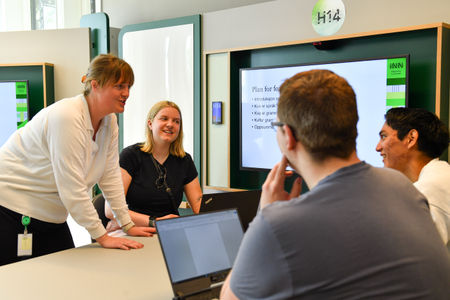 Kvinnelig lærer underviser studenter ved et bord. Foto.