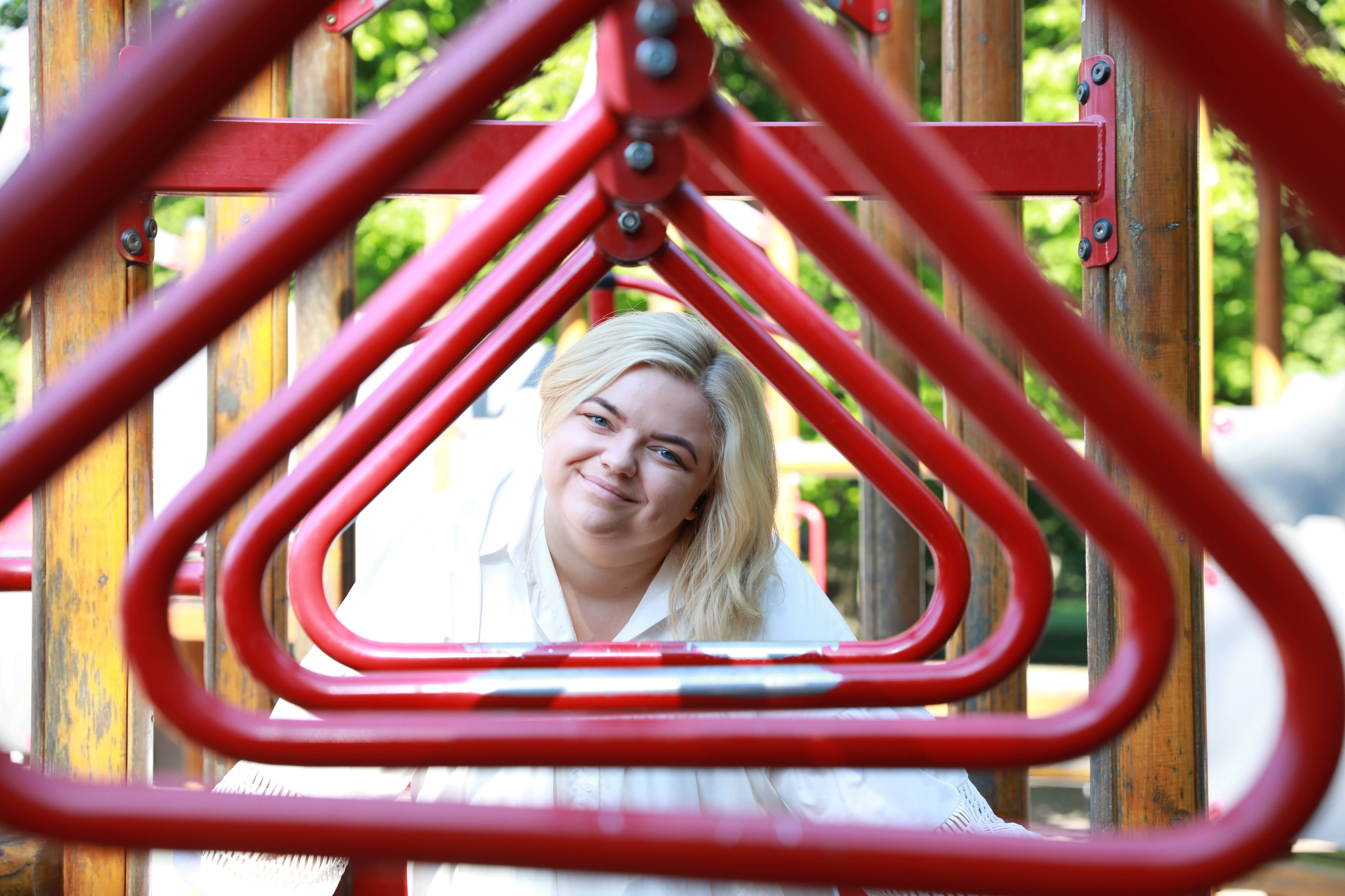 Blond kvinne smiler og ser inn i kamera. Foran henne er det en tunnel røde ringer som rammer inn ansiktet. Foto. 