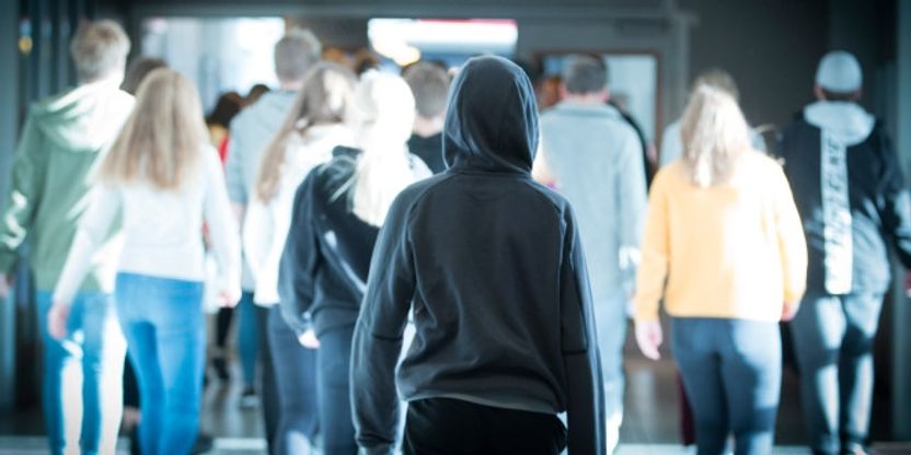 Bilde av en elev bakfra med hette på hodet som står i utgangen av en stor gruppe elever som er på vei inn en dør. Illustrasjonsfoto