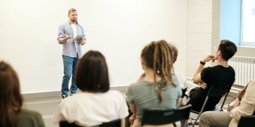 Foto av lærer som står foran elever i klasserom. 