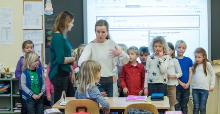 En gjeng barn står samlet med en voksen person foran seg. Foto. 