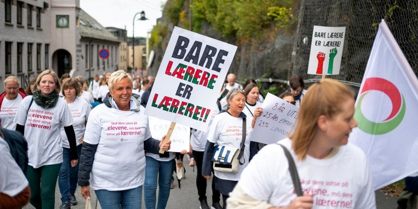 Lærere med hvite streiketskjorter går i tog med plakater "Bare lærere er lærere" 