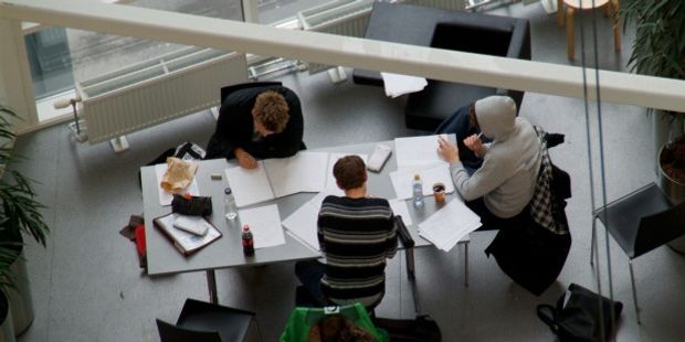 Tre studenter som gjør skolearbeid ved et møtebord. Illustrasjonsfoto.