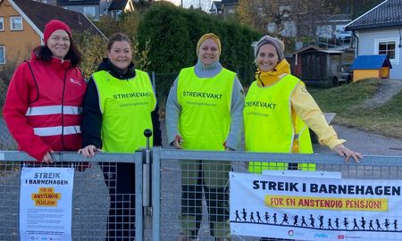 Bilde av 4 streikende i Strai barnehage. De har streikevester, banner og plakater.