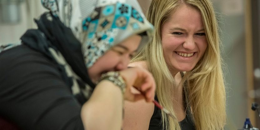Nærbilde av to videregående elever som ler. Hun fremste har på seg et fargerikt sjal på hodet og holder hånden foran munnen. Hun bakerste har langt lyst hår og gliser.