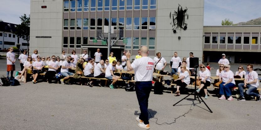 En gjeng lærere er samlet i streikeskjorter foran Gimle oppveksttun skole i Bergen. Foran dem holder Steffen Handal en mikrofon og fremfører sin appell. Foto: Paul S. Amundsen/Utdanningsforbundet.