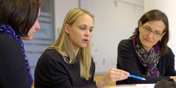 Kvinne blant to andre kvinner holder en penn. Foto.