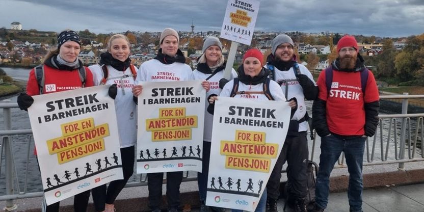 Sju streikende fra Utdanningsforbundet og Fagforbundet med plakater og t-skjorter med påskriften "Streik i barnehagen - for en anstendig pensjon!" Foto.