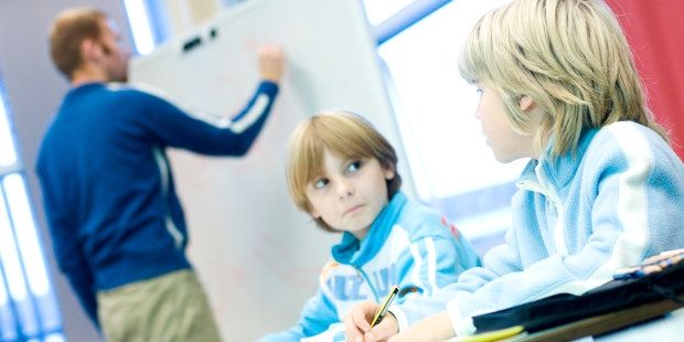 Bilde av to elever som ser på hverandre foran lærer som skriver på tavla.