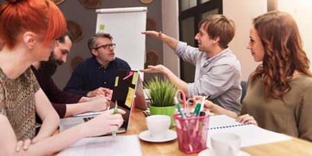 Samtale mellom fem personer rundt et bord på en arbeidsplass. Foto.