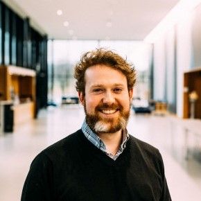 Bilde av J. Parcival Kjæret. Hvit mann med skjegg og krøllete hår, som smiler mot kamera. Foto: Adrian Castillo.