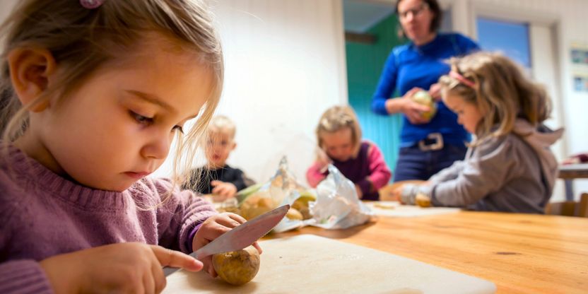 Barn i aktivitet i en barnehage, jente i forgrunnen, flere barn og voksen i bakgrunnen. FOTO.