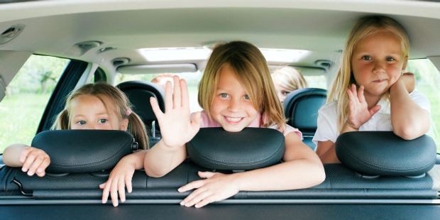 Tre barn titter ut av bakvinduet på en bil. Foto