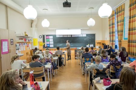 En gruppe elever som sitter i et klasserom med læreren som står foran tavla. Foto. 