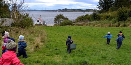 Barnehagebarn som går på en grønn slette. Foto.