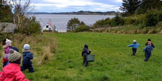 Barnehagebarn som går på en grønn slette. Foto.