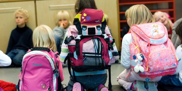 Barn som sitter i en ring på et gulv. Noen med ransel på. Foto.