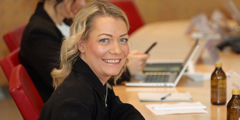 Sandra Borch ser i kamera og smiler. Hun sitter ved et møtebord.