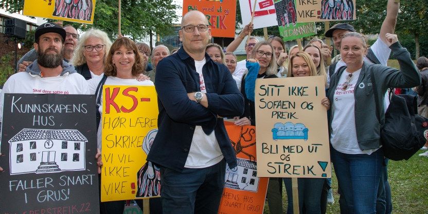 Steffen Handal står foran demonstrerende lærere med ulike hjemmelagde plakater som omhandler lærerstreiken.