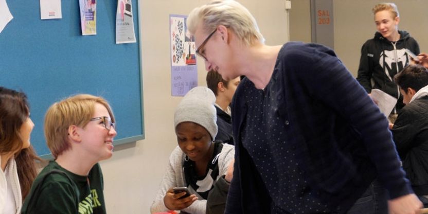 en rektor står ved et bord der elever sitter og alle smiler