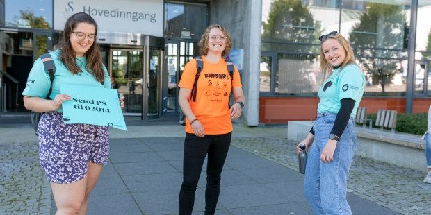 Tre blide kvinner står klare til å ta imot nye medlemmer. Kvinnen til venstre har langt brunt hår med blå t-skjorte og holder oppe et skilt det står Bli medlem på. Kvinnen i midten har halvlangt brunt hår, oransje t-skjorte og smiler til kamera. Kvinnen til høyre har også en blå t-skjorte på og er glad. Foto.