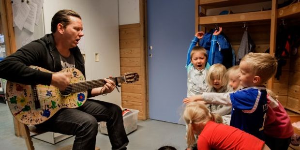 Barnehagelærer som spiller gitar for barn. Foto.