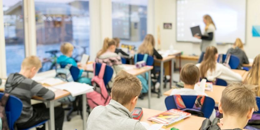foto fra et fullt klasserom der elevene ses bakfra, ved tavla foran ses en kvinnelig lærer