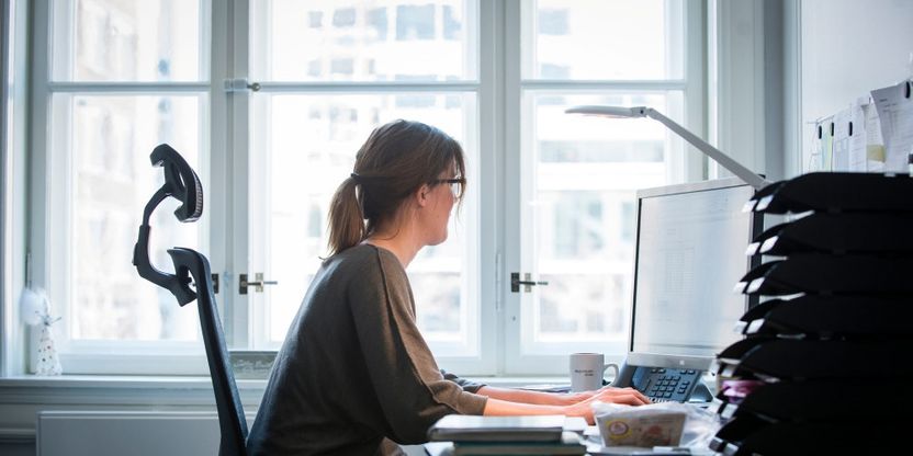 Kvinne sitter foran en PC og arbeider. Hun er på et kontor eller hjemmekontor.