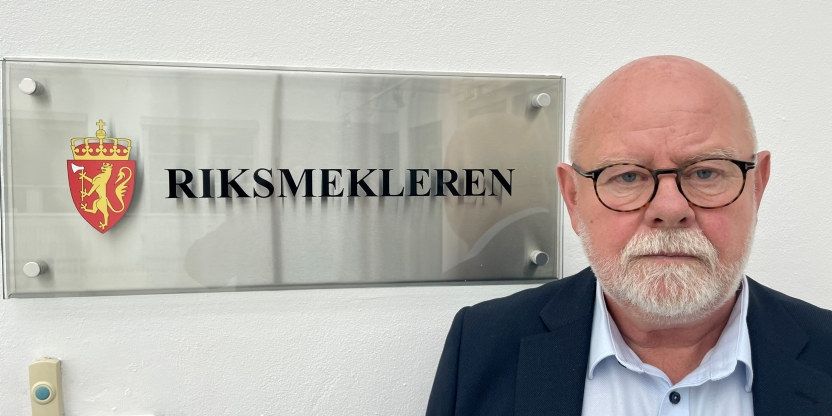 Utsnitt av Utdanningsforbundets nestleder Terje Skyvulstad foran Riksmekler-skiltet. Skyvulstad ser alvorlig ut med briller og hvit skjegg.