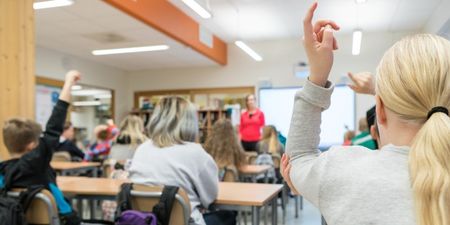 Elever i et klasserom sett bakfra. Flere av elevene holder hånda i været. Illustrasjonsfoto.