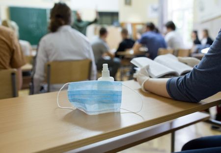 Close up of mask and disinfectant on school desk beside student with gloves after pandemic. Safety and recommended measures