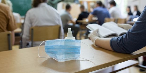 Close up of mask and disinfectant on school desk beside student with gloves after pandemic. Safety and recommended measures