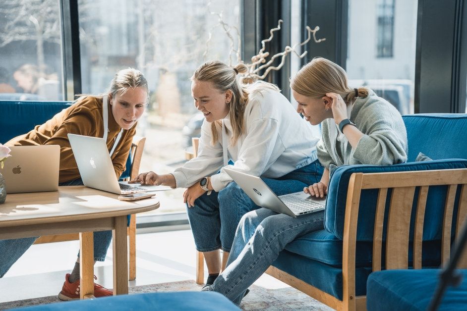 En studentgruppe som samarbeider. Sitter i sofa og ser på felles dokument på et bord. Foto. 