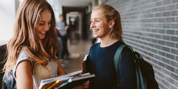 to jenter i tenårene smiler mot hverandre i skolekorridor