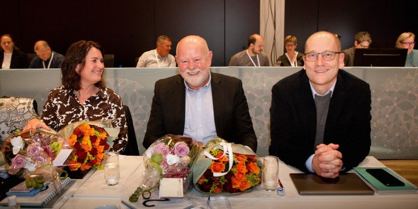 Hege Valås, Terje Skyvulstad og Steffen Handal sitter ved et bord på landsmøtet i 2019 med blomsterbuketter foran seg. De smiler mot fotografen.