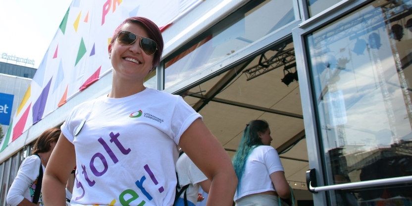 Ann Mari Milo Lorentzen står foran et Pride-telt og smiler. Hun har på seg t-skjorte med skriften "Stolt lærer" på. Det er solskinn og hun har på seg solbriller.