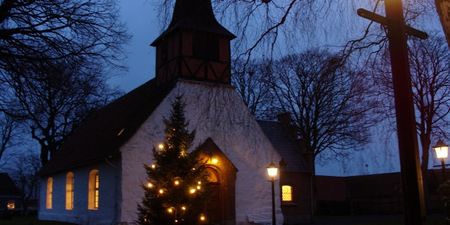 Bilde av en kirke på kveldstid, med et lysende juletre utenfor. 