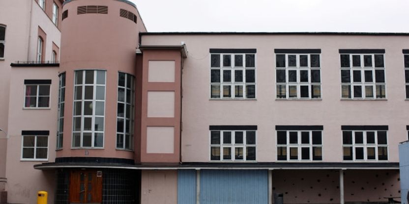 Bilde av et nøytralt skolebygg, hvor du kan se en fargeløs vegg med vinduer, samt en asfaltert skolegård i forkant.