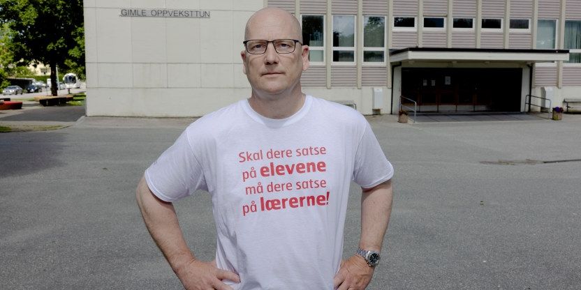 Bilde av Steffen Handal foran Gimle oppveksttun skole i Bergen. Han har på seg hvit streike T-skjorte hvor det står: Skal dere satse på elevene, må dere satse på lærerne.