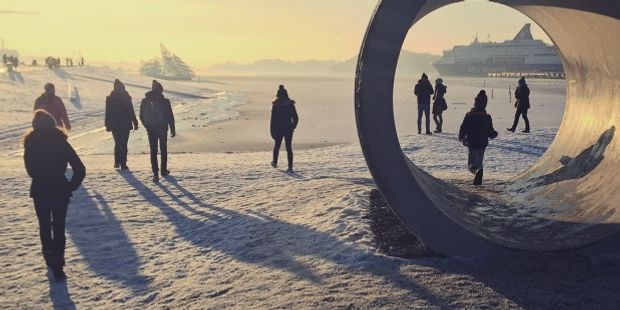 Mennesker ved havna i skarpt vinterlys og lange skygger. Foto.