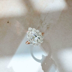 A 14k white and rose gold ring with a pear moissanite center stone and 3mm moissanites on a halo.