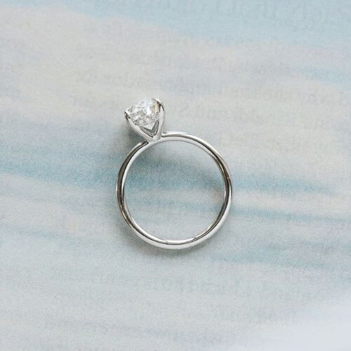 An oval, 14k white gold solitaire featuring a hidden halo of small round diamonds between the claws.