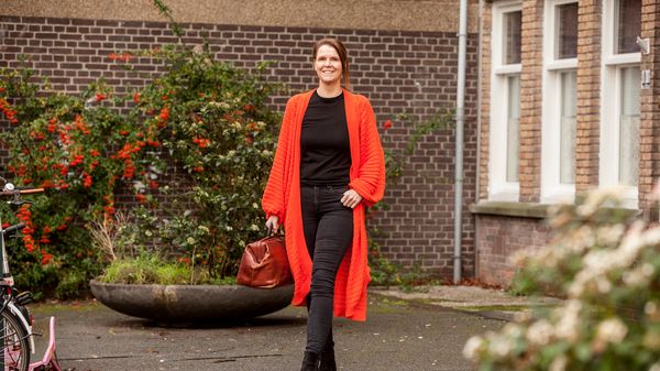 Vrouw met rood lang vest lopend voor pand